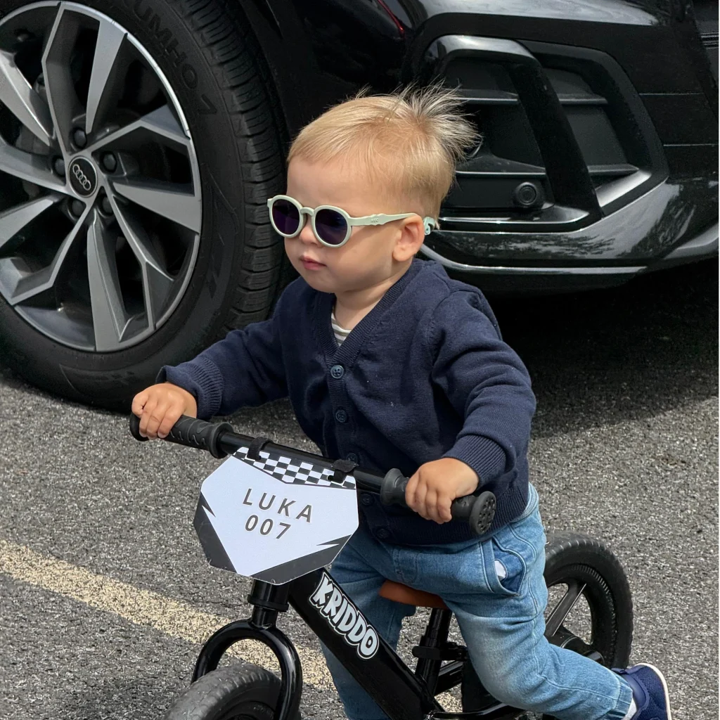 A three-year-old boy wearing KiGO sunglasses is riding a bicycle.