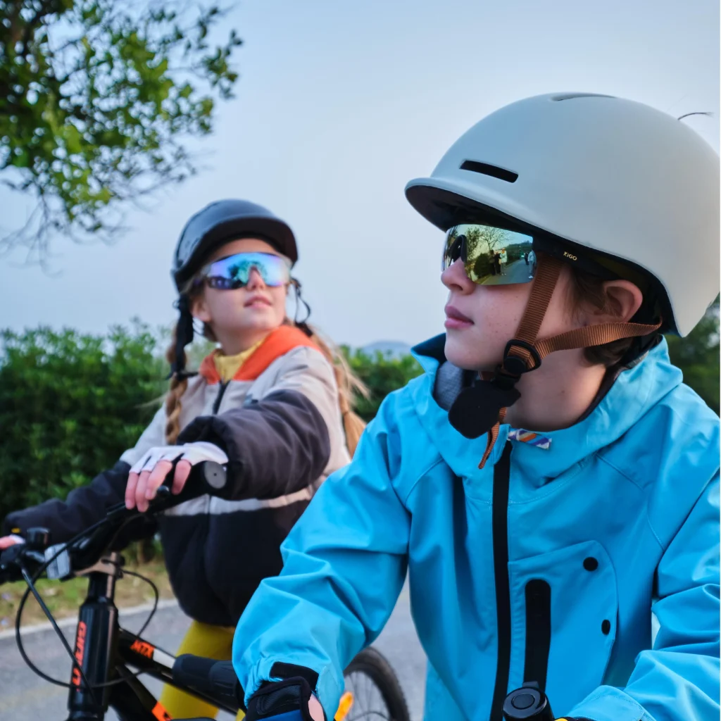 A boy and a girl wearing KiGO sports sunglasses are riding bicycles on the road.