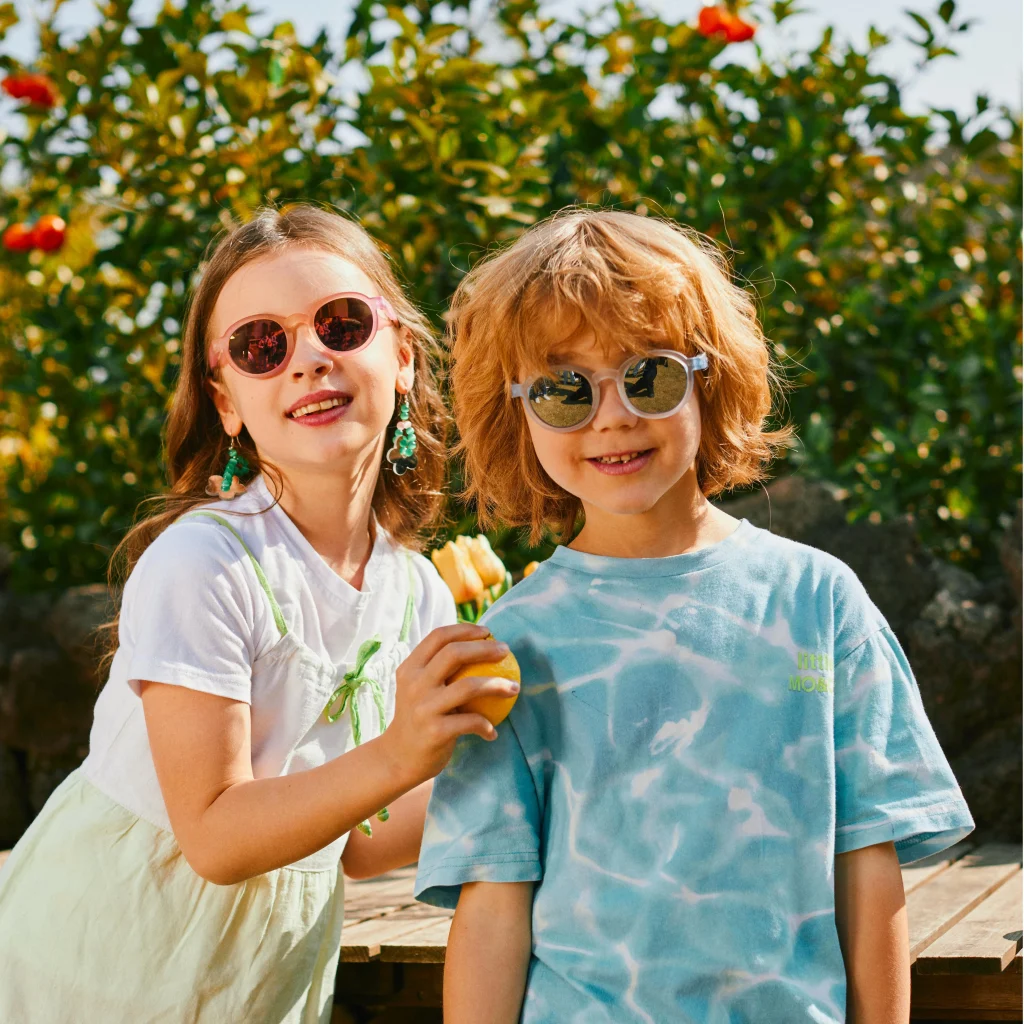 A little girl and a little boy wearing KiGO blenders kids sunglasses stand in front of an orange tree.