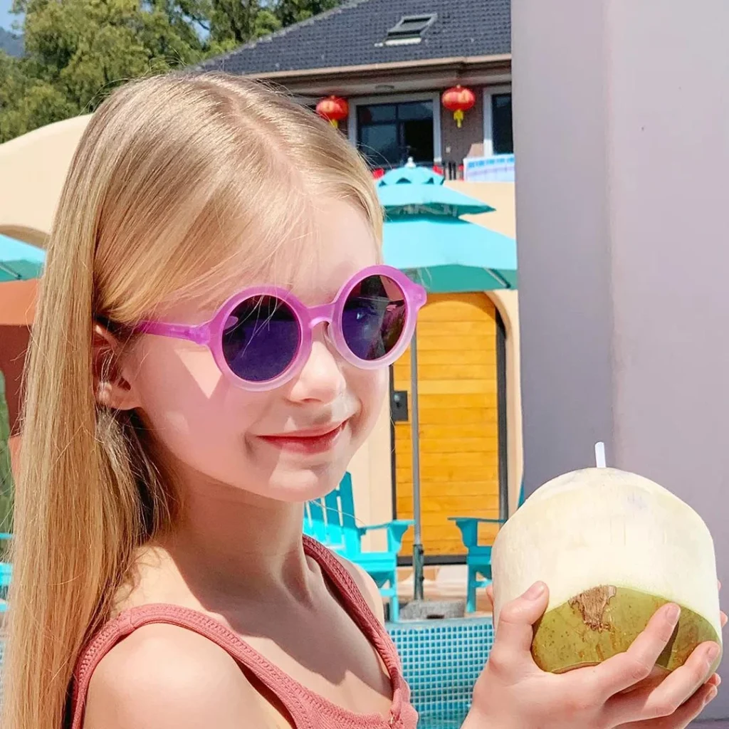 A 7-year-old girl wearing KiGO pink sunglasses is holding a coconut.