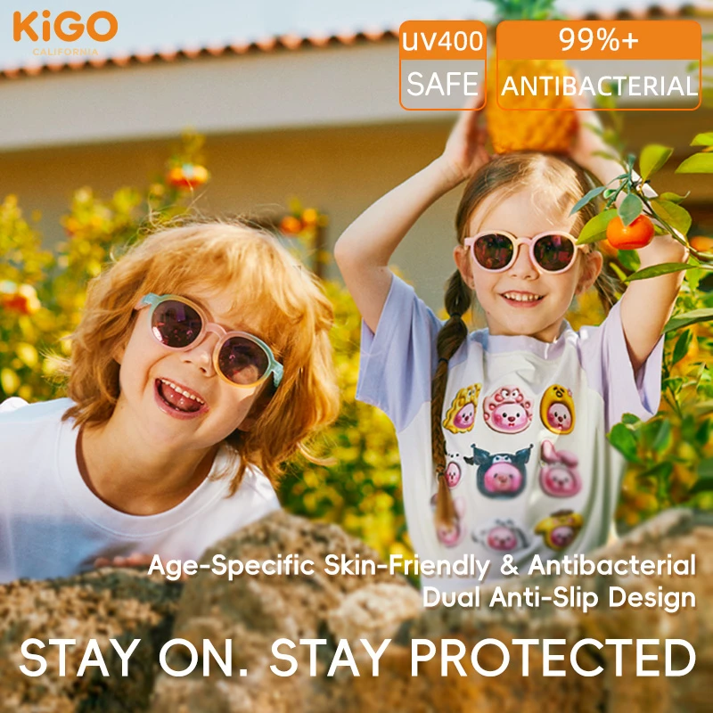 Two children wearing KIGO California sunglasses kids polarized in a sunny, green outdoor setting. Text highlights "UV400 SAFE", "99%+ ANTIBACTERIAL", "Age-Specific Skin-Friendly & Antibacterial Dual Anti-Slip Design", and "STAY ON. STAY PROTECTED", with the brand logo in the top left.