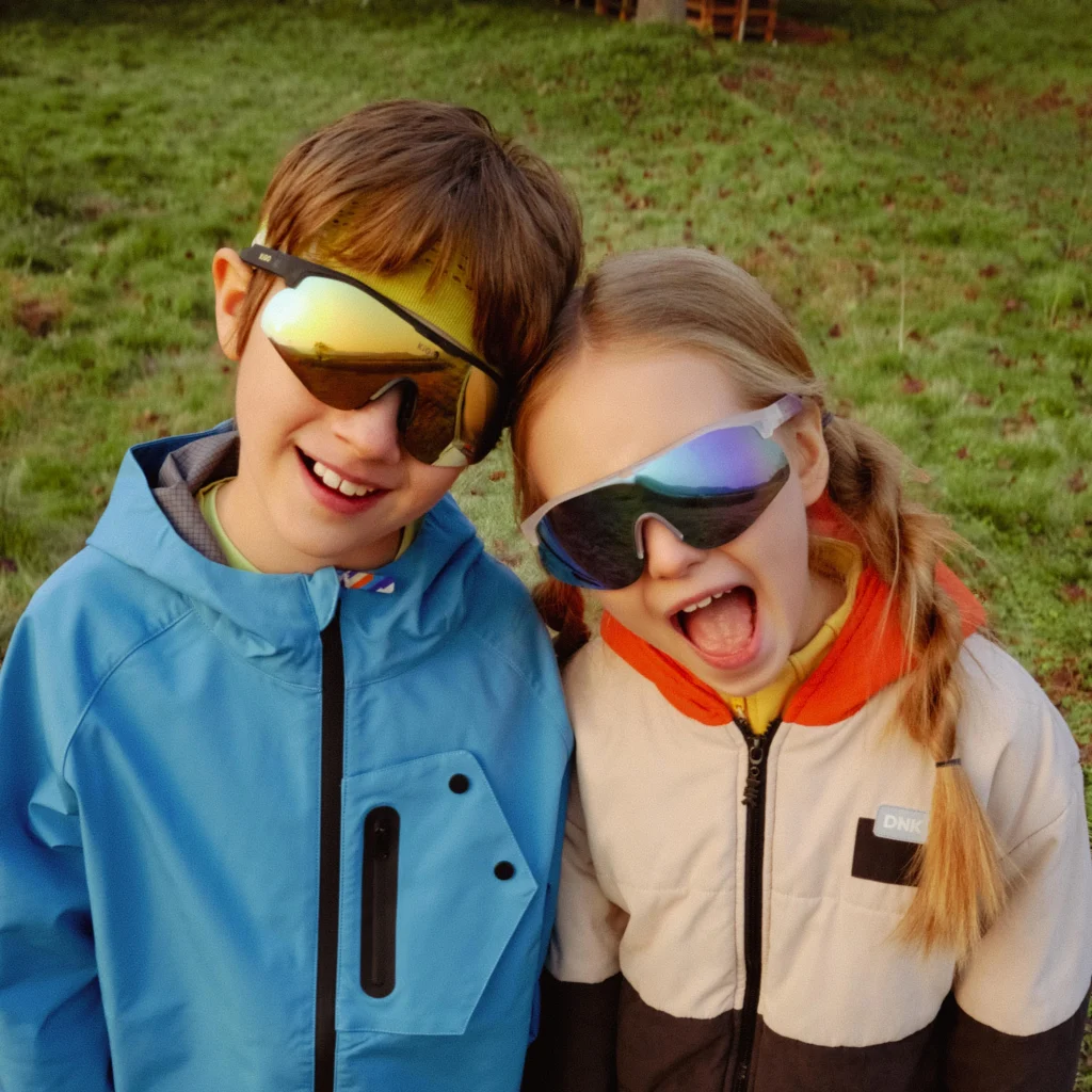 A six-year-old boy and a six-year-old girl are standing on the grass wearing KiGO California spotters kids sunglasses​.