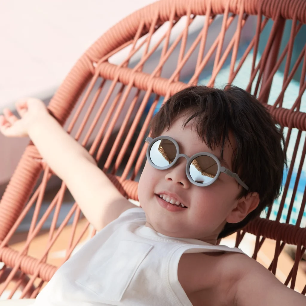 A 5-year-old boy wearing KiGO sunglasses sits in a chair with his arms outstretched.
