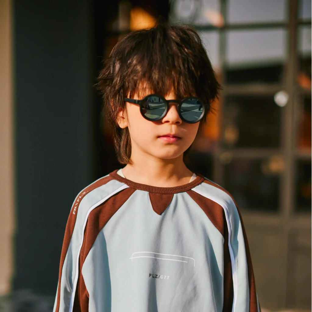 A five-year-old boy wearing black KiGO boys kids sunglasses​ stands on the street.
