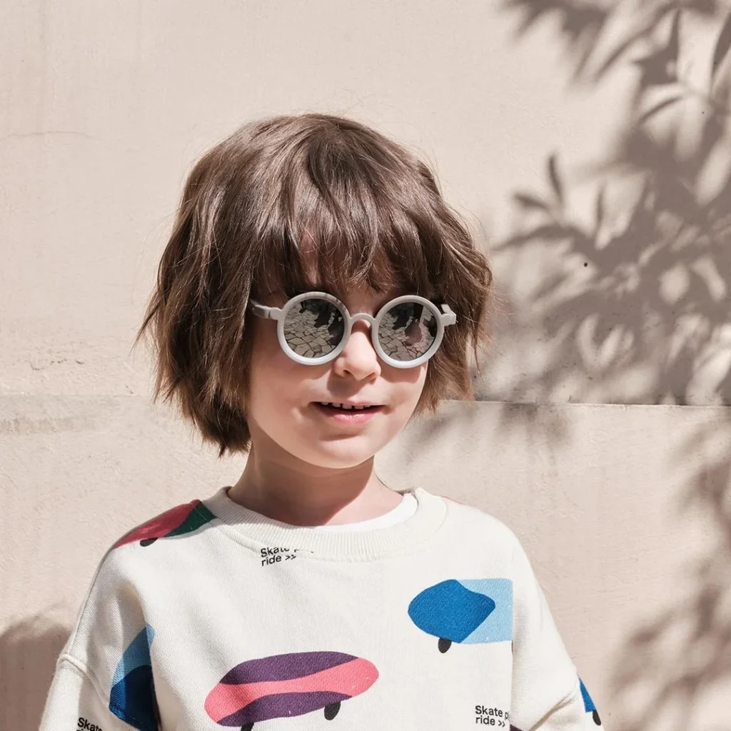 A six-year-old boy wearing KiGO sunglasses stands in front of a gray wall.