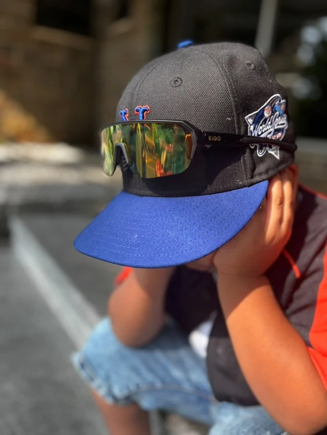 A little boy wearing KiGO California sport sunglasses kids sits at the door of his house ready to go out for exercise.