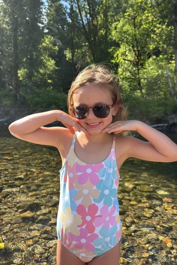 A 6-year-old girl wearing KiGO California kids uv sunglasses is standing in the stream and smiling happily.