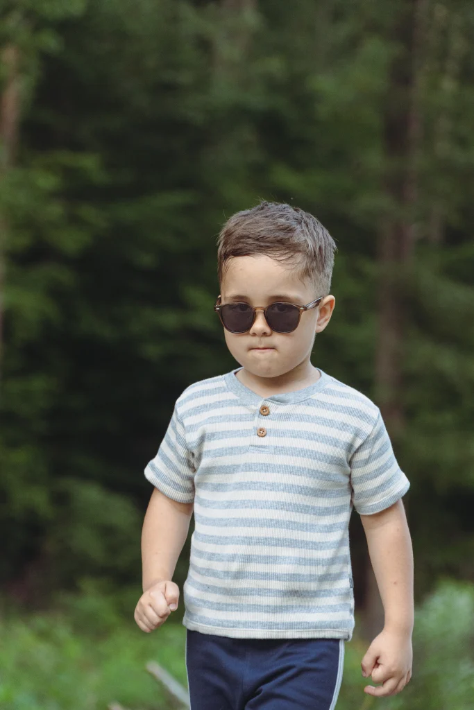 A handsome boy wearing KiGO California polaroid kids sunglasses walks along a forest path.