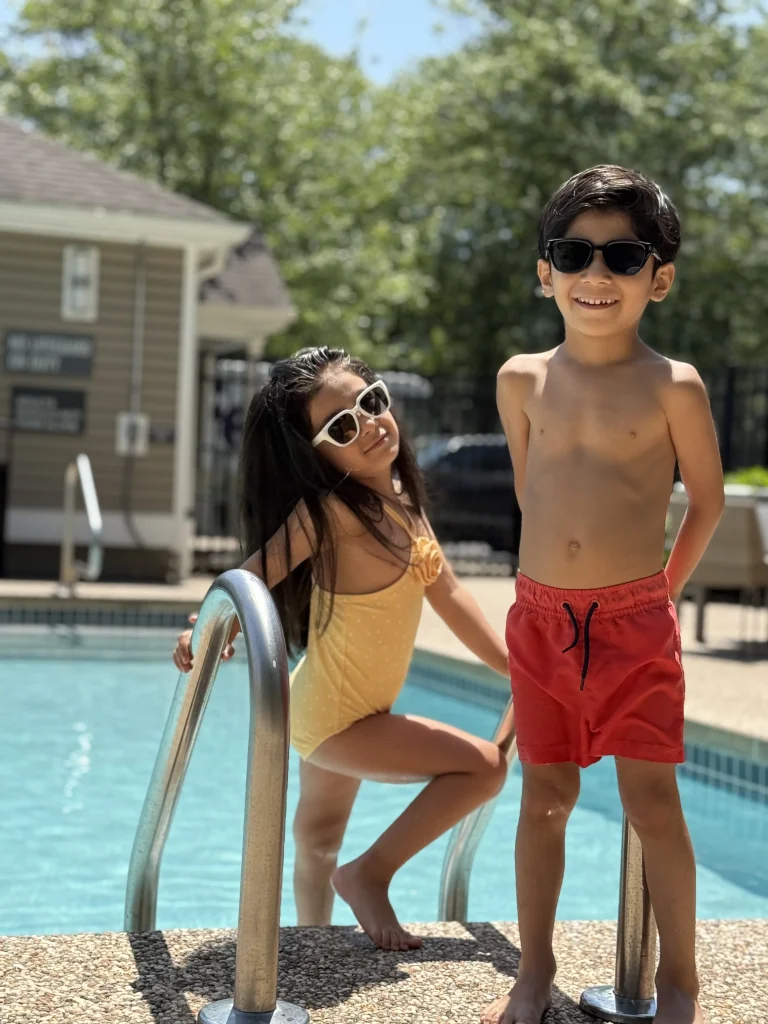 A brother and sister play by the pool wearing KiGO California kids black sunglasses and kids white sunglasses.