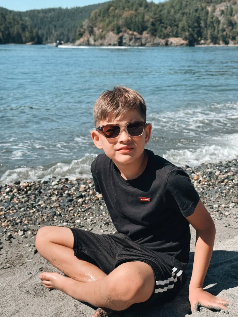 A litle gentlemen wearing KiGO California Brown color good kids sunglasses for 6-12 years sitting on the seaside.
