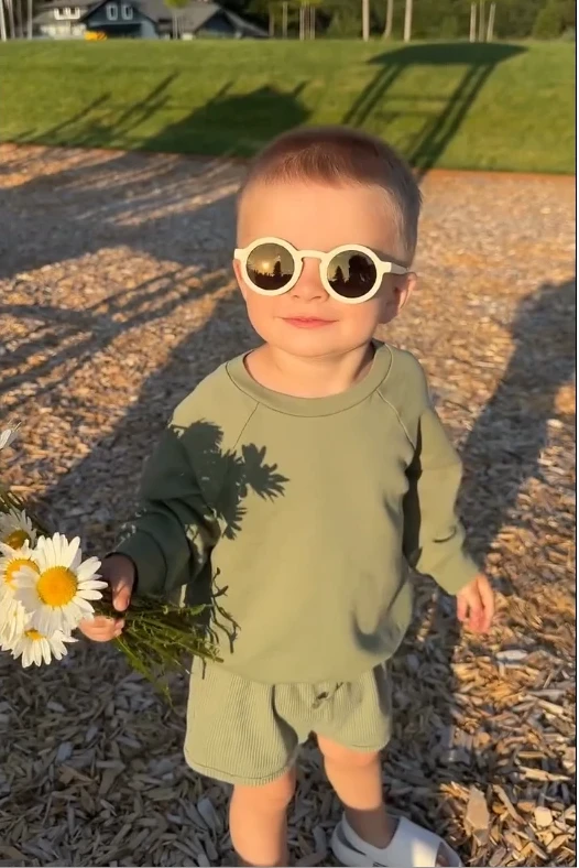 A little boy holds a bunch of flowers in his hand and wears KiGO California sunglass kids, looking up at the sun.
